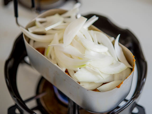 玉ねぎとパクチーの根を加えて蓋をして5分蒸し焼きにします